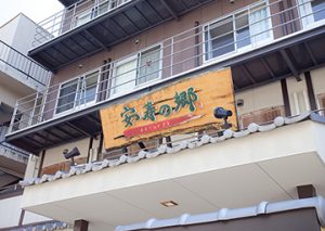 木造建物の外観。黄色の暖簾が掛かった施設の正面。複数階建て。